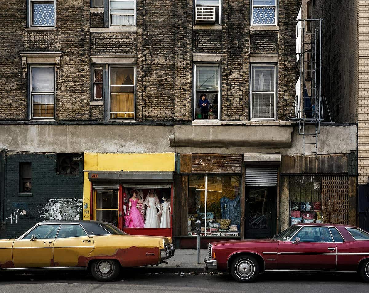 A bridal shop and other stores with two cars parked in front, in New York. 1980