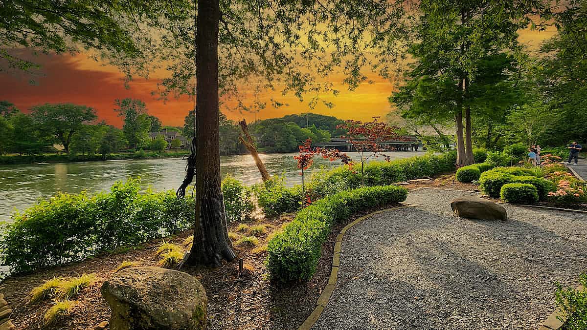 A gorgeous spring landscape along the Chattahoochee River with lush green trees, grass and plants and colorful flowers with powerful clouds at sunset at Ray’s on the River in Sandy Springs, Georgia.