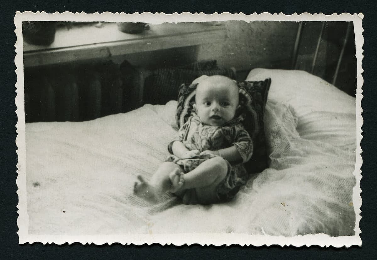 An antique photo shows small happy child lying on the bed.