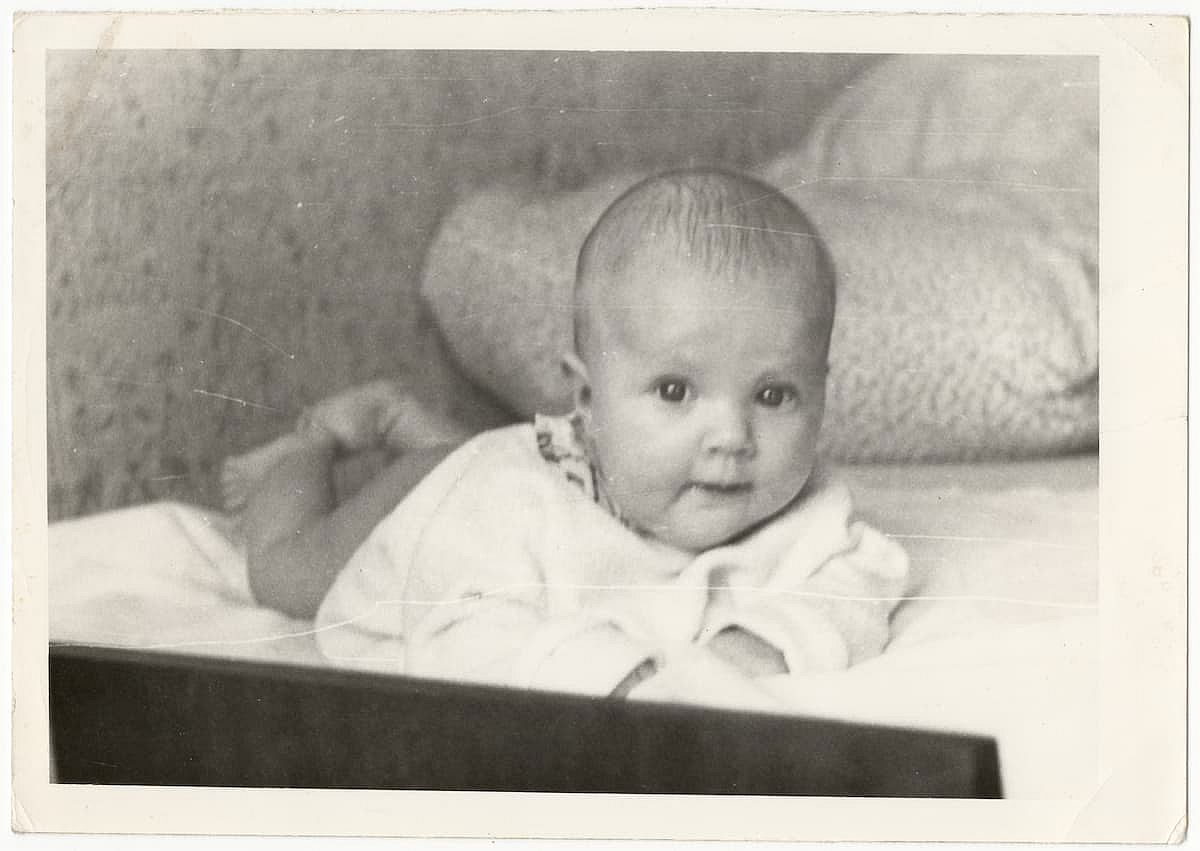 Old cute photo of a baby on a bed. Vintage black and white photo, slightly yellowed from time to time,