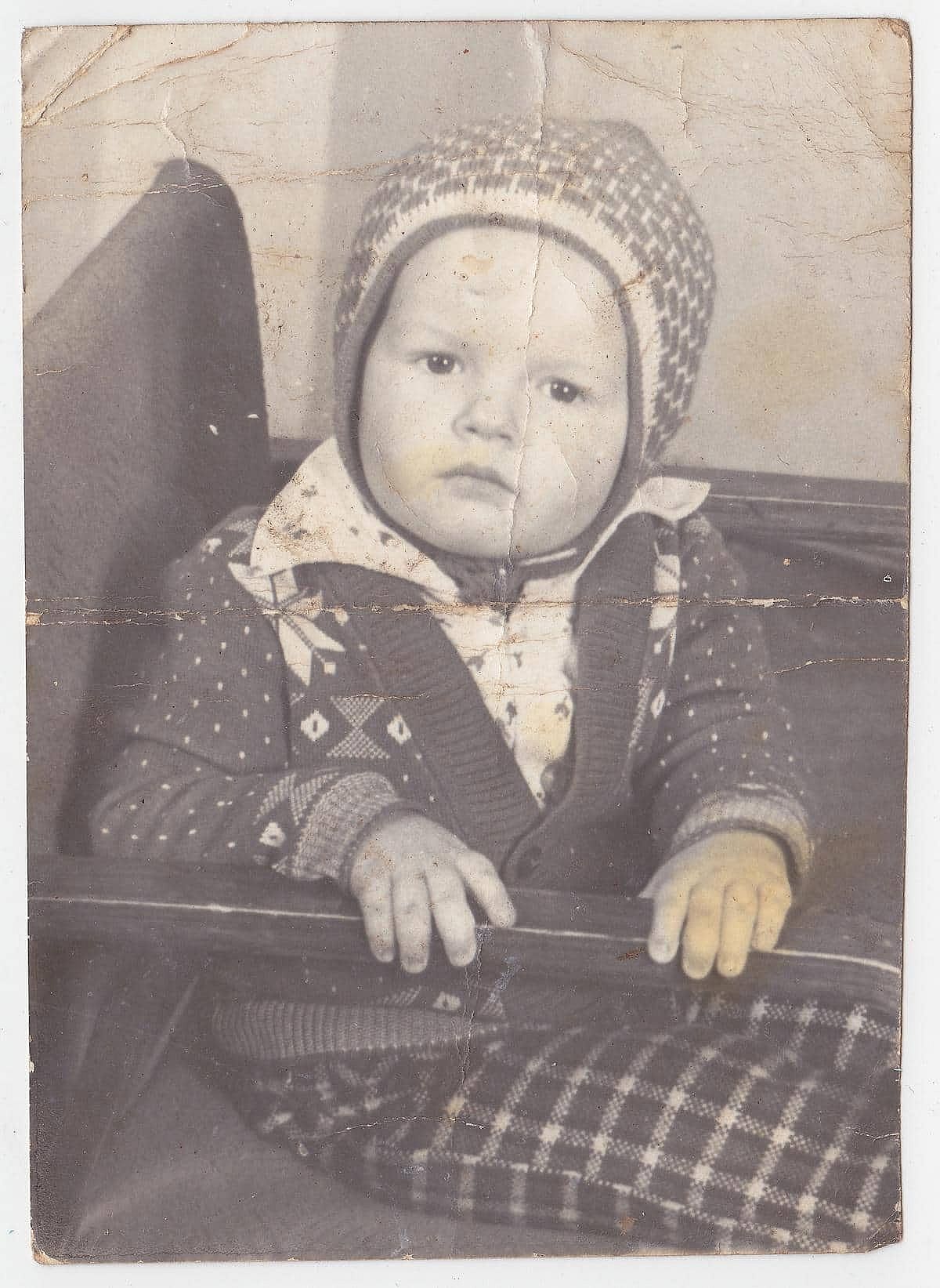 Vintage black and white photo from yesteryear. In the photo there is a child sitting in an old Soviet chair.