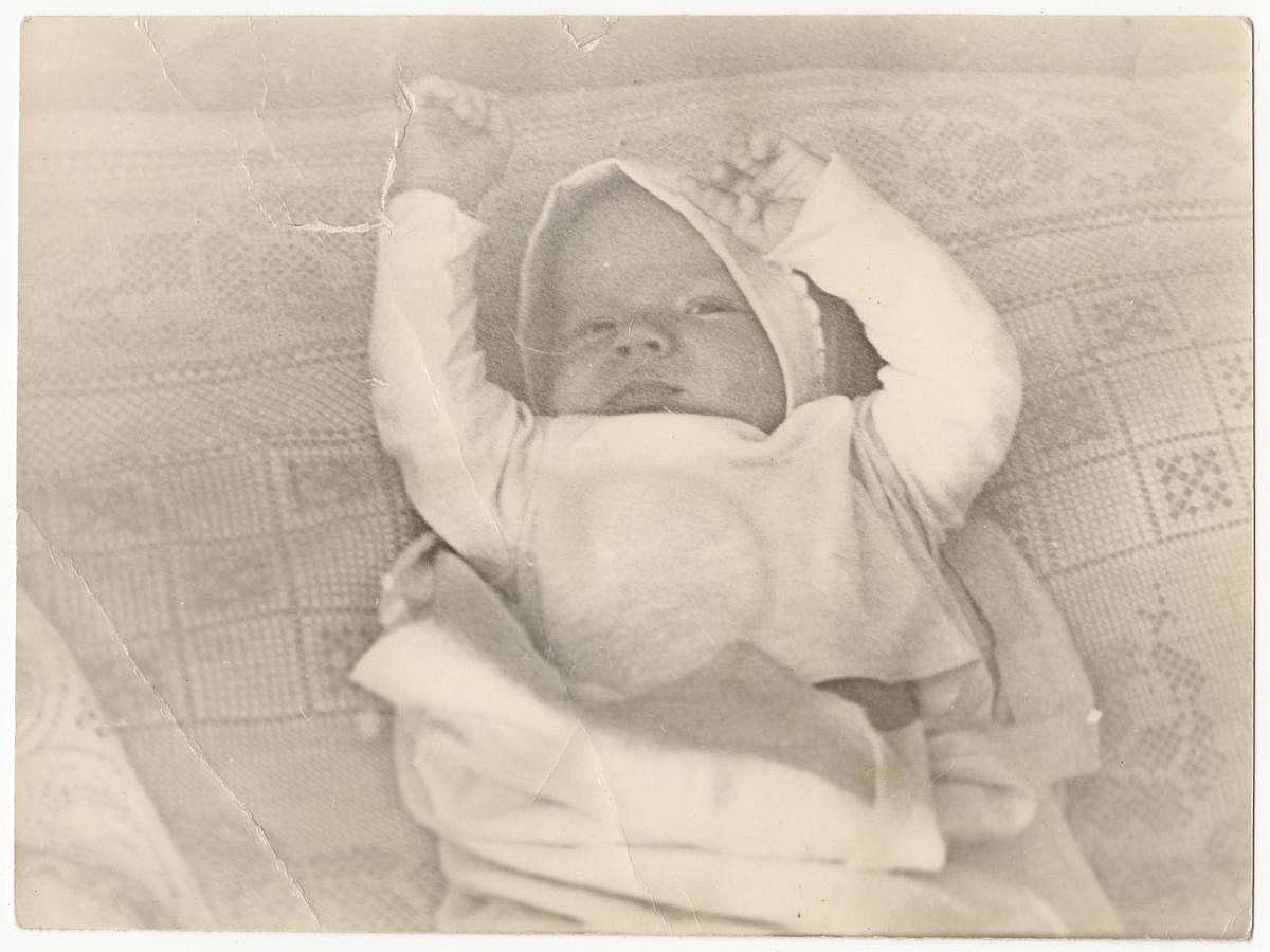 An old cute photo of a baby on a bed. Vintage, not very clear black and white photo, slightly yellowed with time.