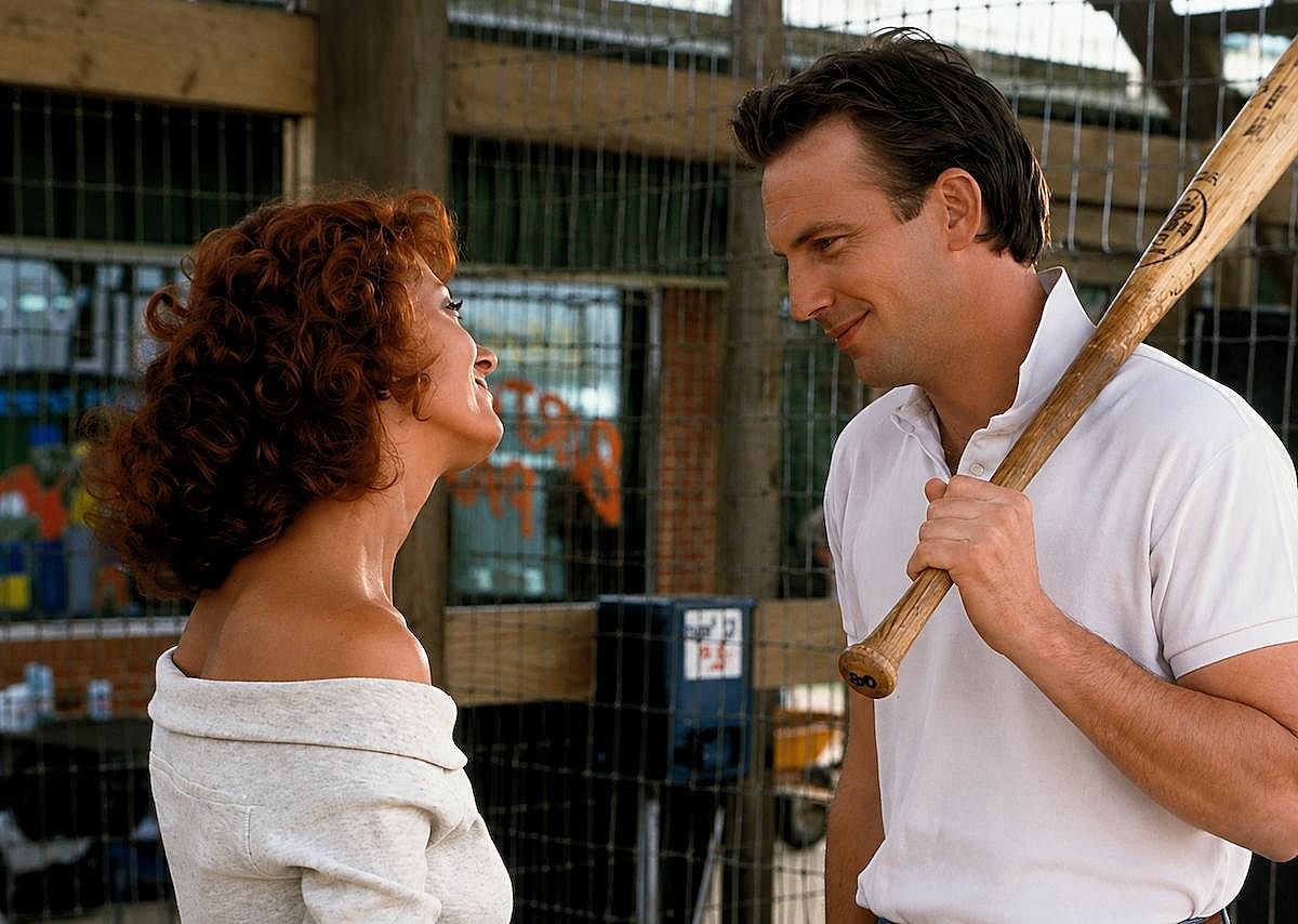 Susan Sarandon and Kevin Costner smiling at each other while holding a baseball bat in Bull Durham