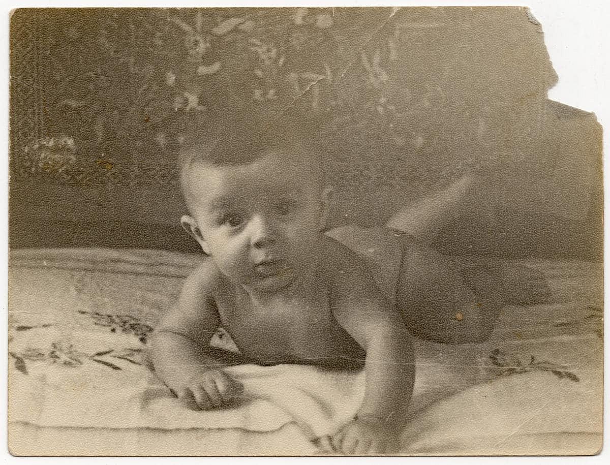 A vintage photograph of a baby crawling on a bed. The photo has a pleasant vintage feel