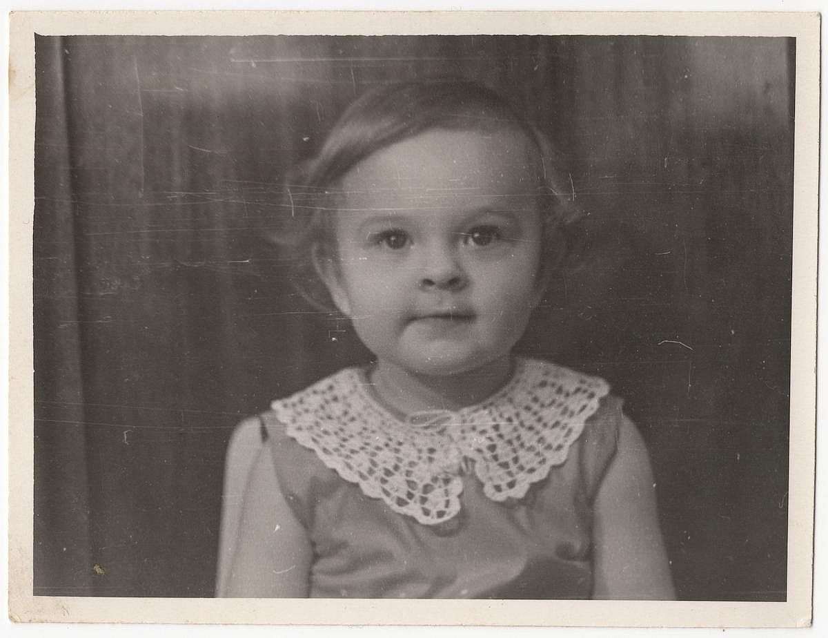 Vintage photo of a cute little girl indoors. Old, slightly yellowed with time, black and white textured photo.