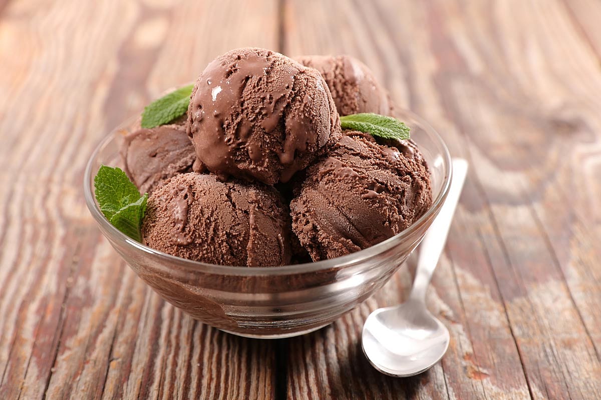 A bowl of chocolate ice cream with a few mint leaves sprinkled around.