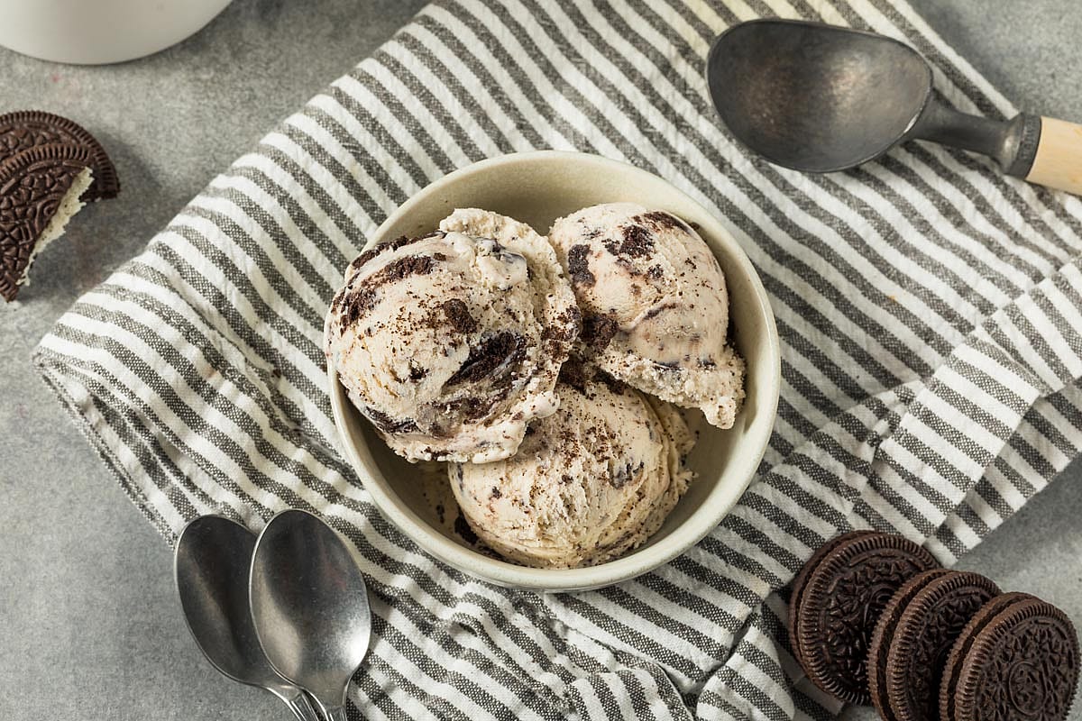 Cookies and cream ice cream bowl surrounded by Oreo cookies and spoons.