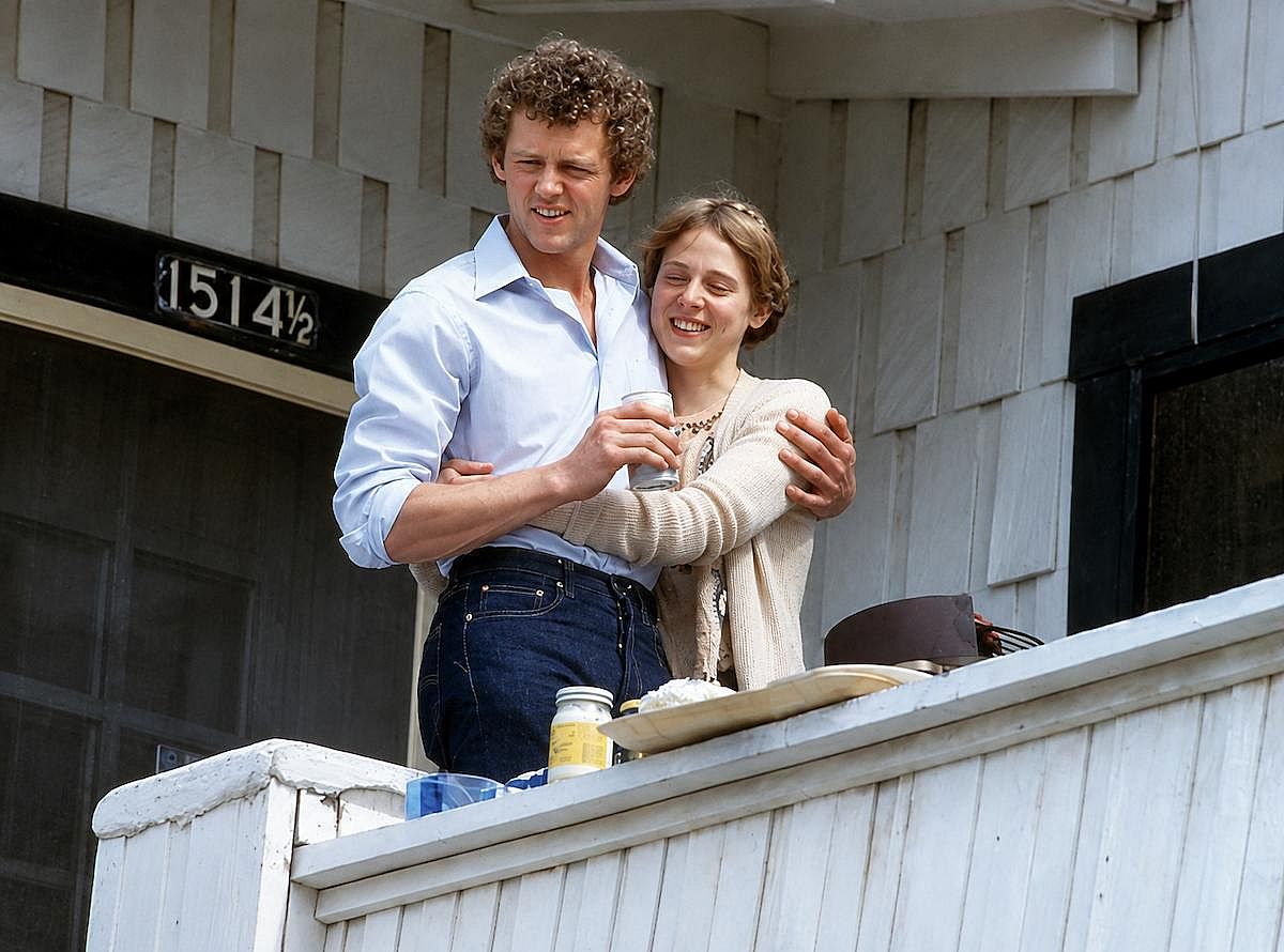 David Morse hugging Amy Wright while holding a can on a balcony, in Inside Moves (1980)