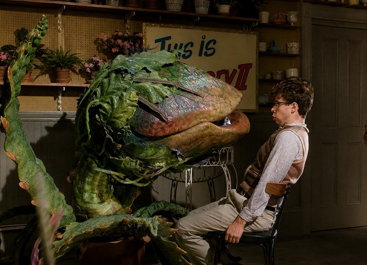 Rick Moranis sitting in front of a monster plant in Little Shop of Horrors (1986)