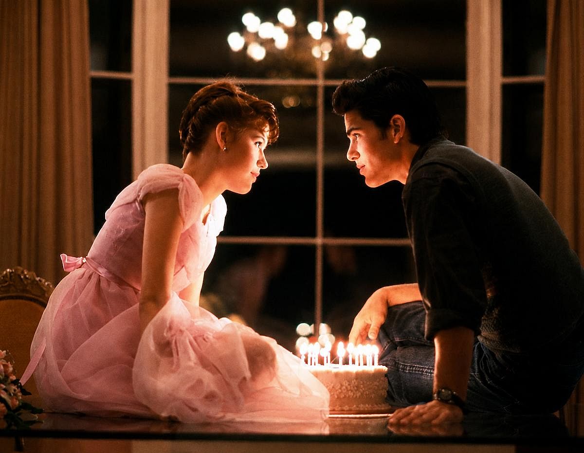 Molly Ringwald and Michael Schoeffling leaning to each other with a birthcake in the middle, the iconic scene of Sixteen Candles 