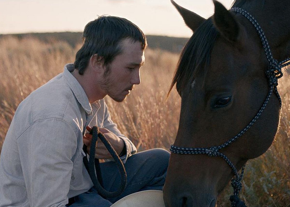 A man kneeling down to a horse.
