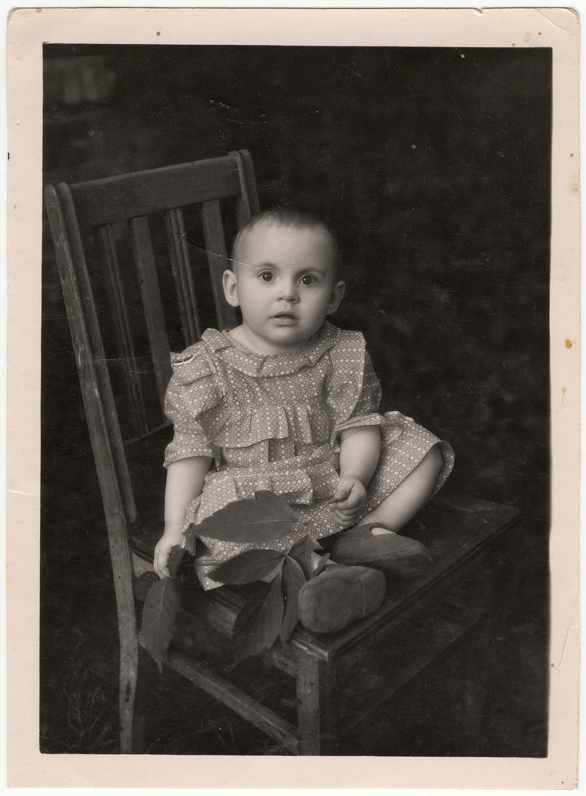 Vintage photo of a little girl sitting on a chair. Old, yellowed black and white photograph taken in the Soviet Union.