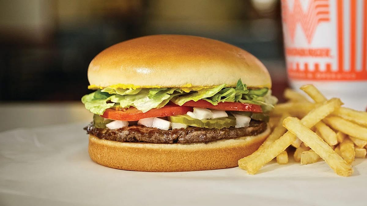 A Single Whataburger on a table next to some french fries.