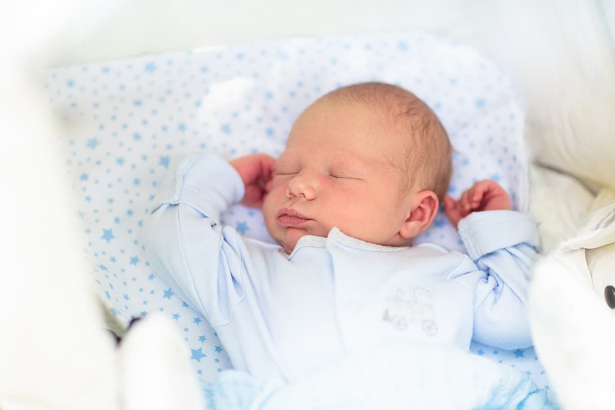Newborn baby sleeping in white stroller on a walk in summer park. New born child napping outdoors on hot sunny day. Infant in a city buggy. Kids sleep in pram. Close up portrait of cute little boy.