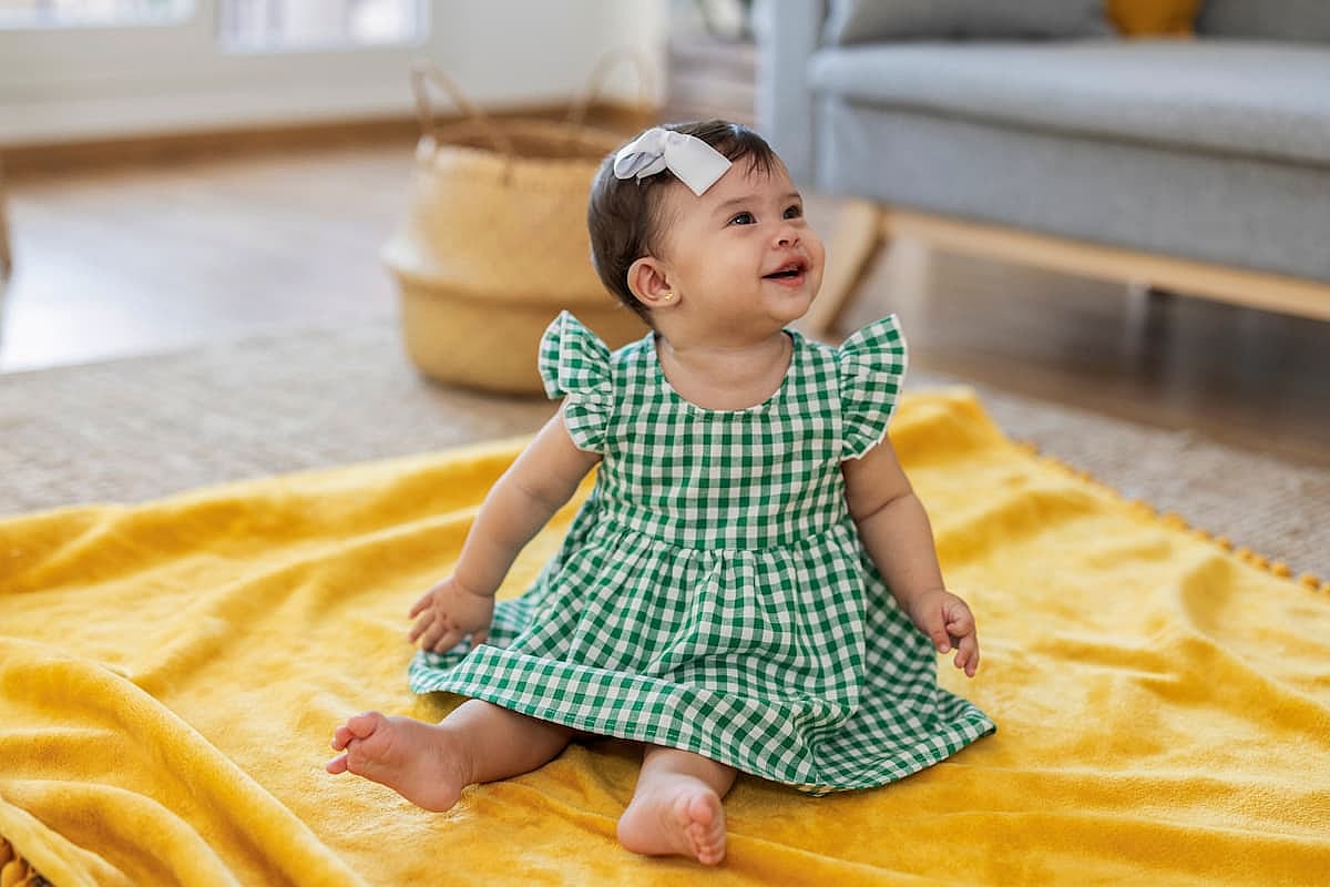 Latina baby girl sitting on a rug on the floor smiles as she looks at her parents