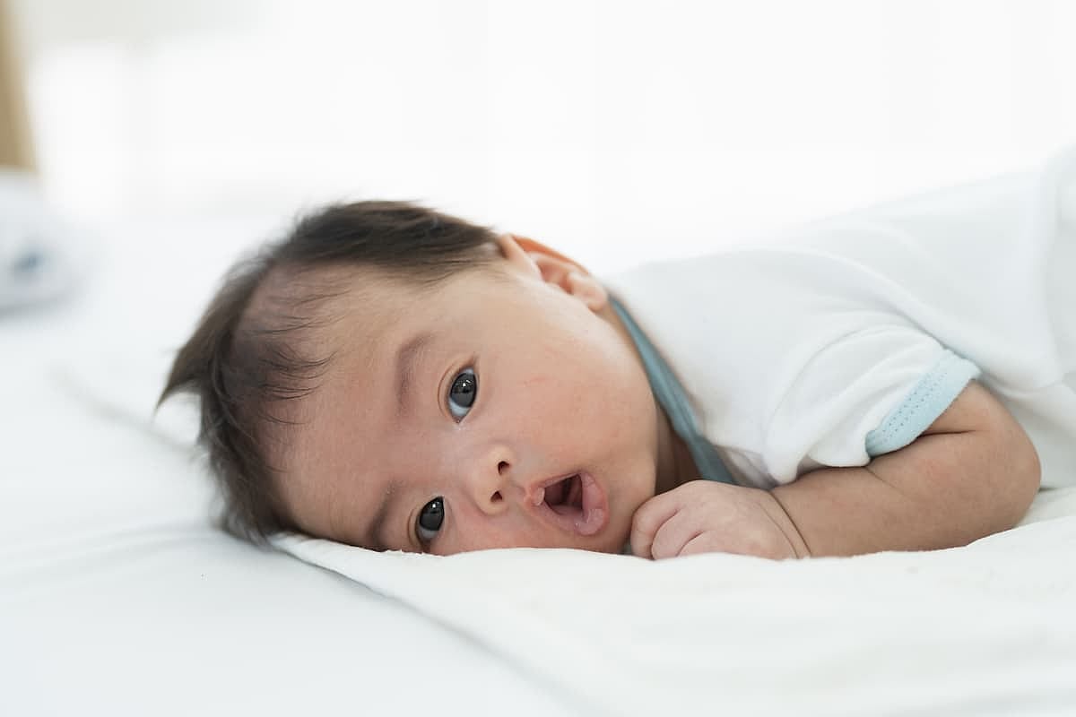 Newborn baby sleeping on white bed. Infant lying on white bed. Asian newborn baby sleeping in prone position. Asian infant