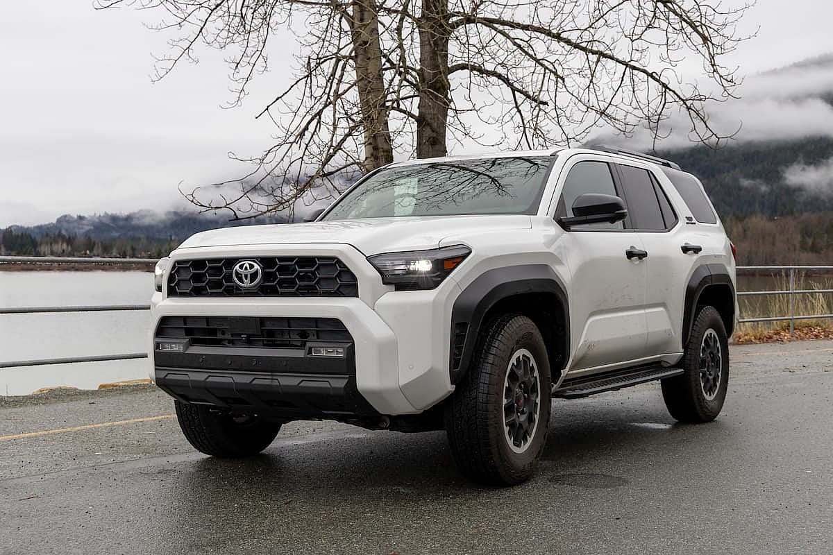 White Toyota 4Runner 2025 parked on a wet mountain road beside a calm lake, surrounded by misty forests and mountains.