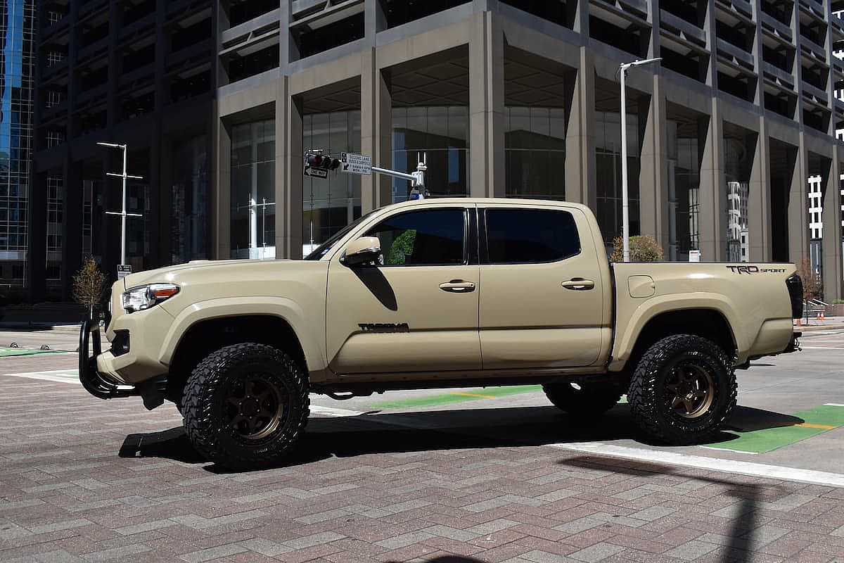 A beige Toyota Tacoma pick-up truck, cruising in the downtown financial district. The office building makes a perfect background which compliments its color.