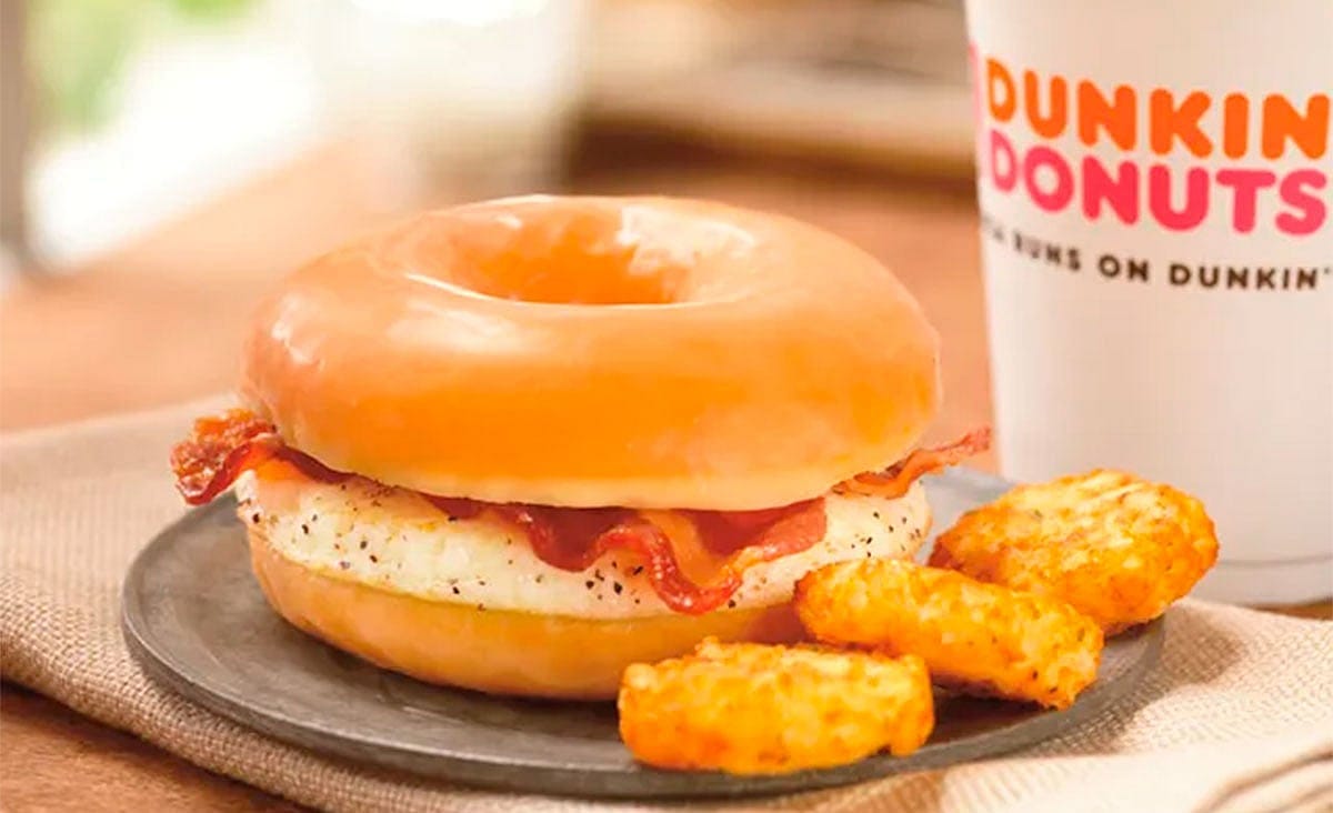 Dunkin’ bacon and egg sandwich on a glazed doughnut, served with hash browns and a coffee cup.