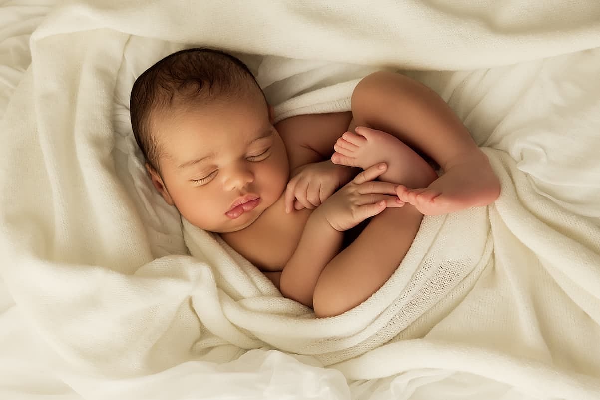Cute little sleeping African biracial newborn baby sleeping on a white soft blanket