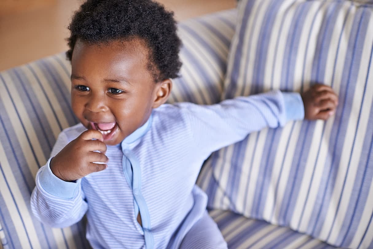 Baby, smile or sofa as play, fun or game for leisure and playing, growth as relax, learn or humor. Excited, black boy child or laugh as curious confidence for motor skill coordination or development