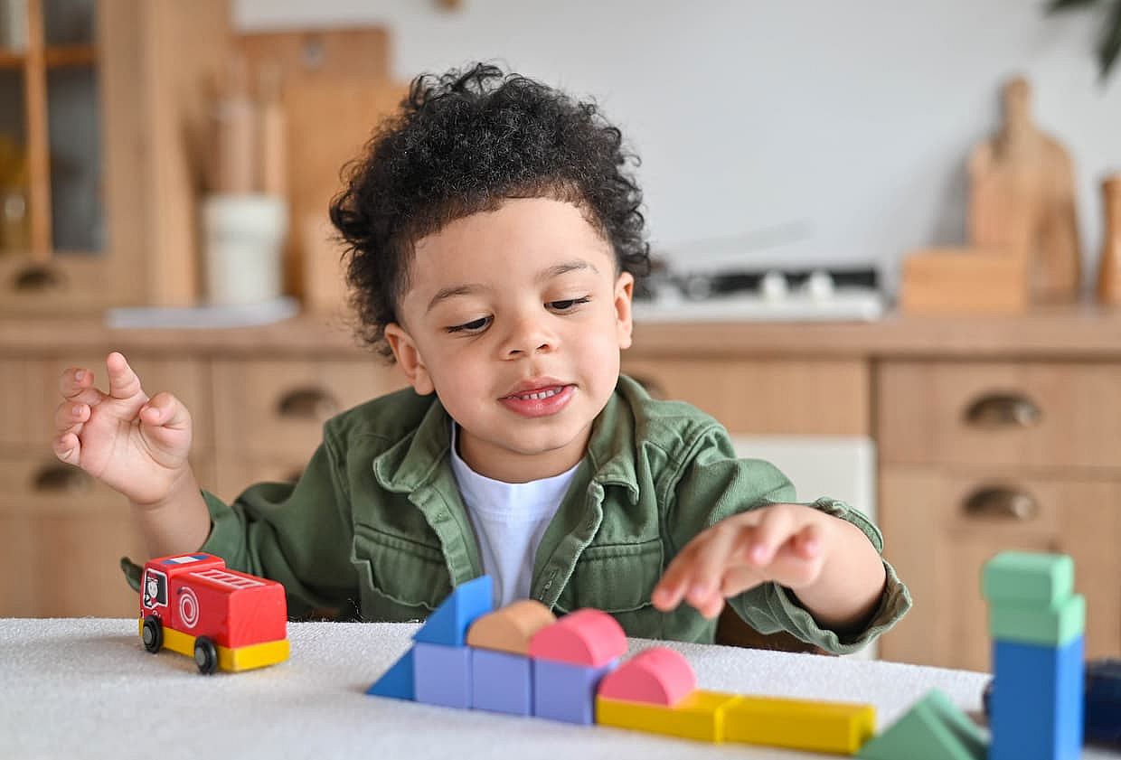 Happy little african american boy with bushy curly hair playing with colorful wooden blocks, enjoying table games playing alone at home kitchen , close up