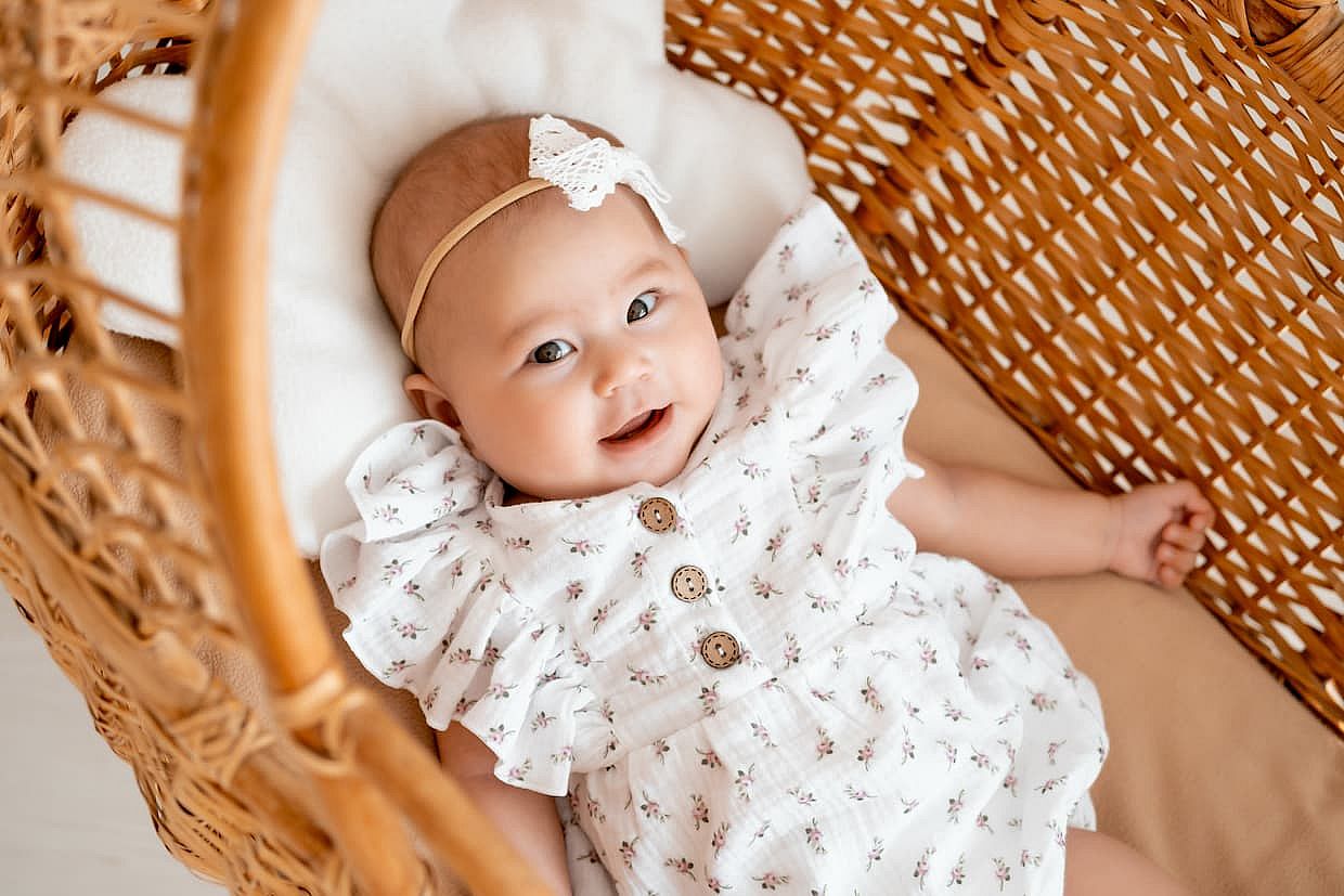 Asian baby girl in a wicker crib goes to bed, a small child smiles or laughs.