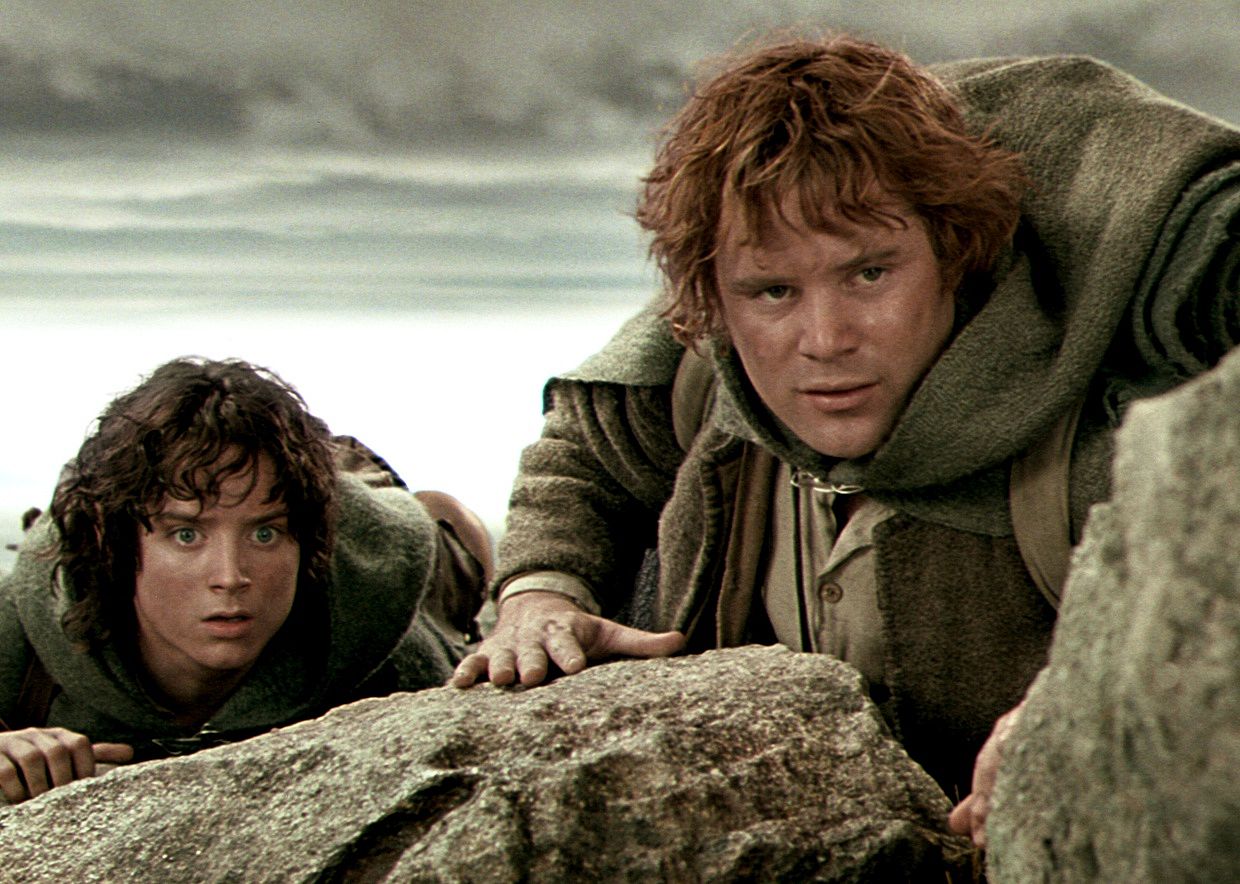 Sean Astin and Elijah Wood peering over rocks.