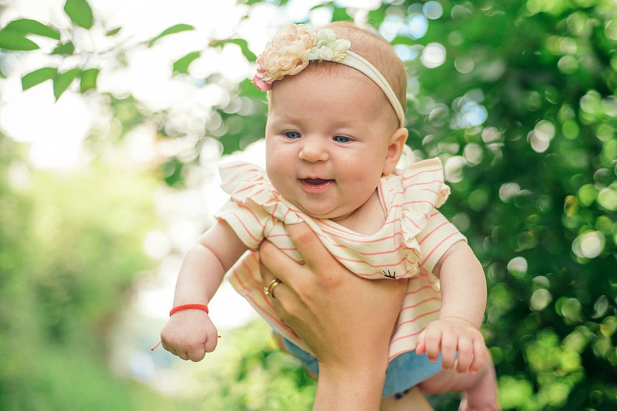 Happy baby in parents hands. Baby girl family bonding outside. Parent and baby. Baby happiness and care.