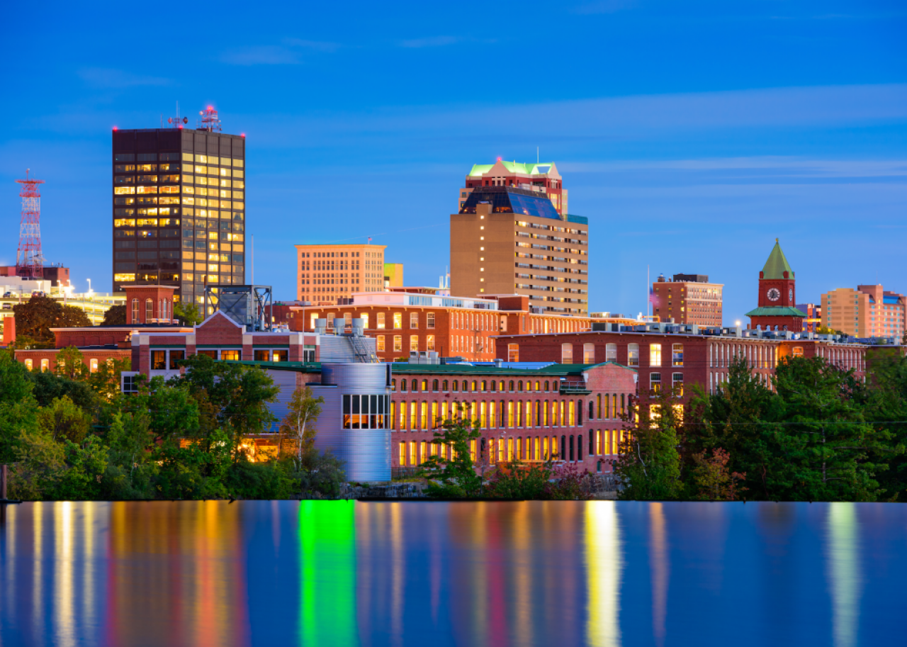City buildings at night with a reflective pond in the foreground.