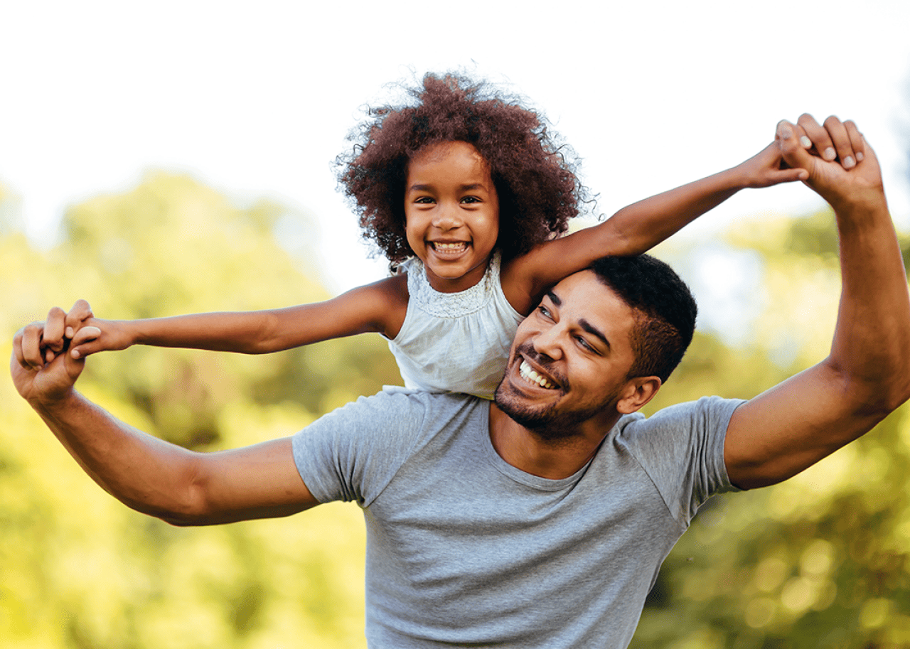 Father carrying daughter on shoulders in park.