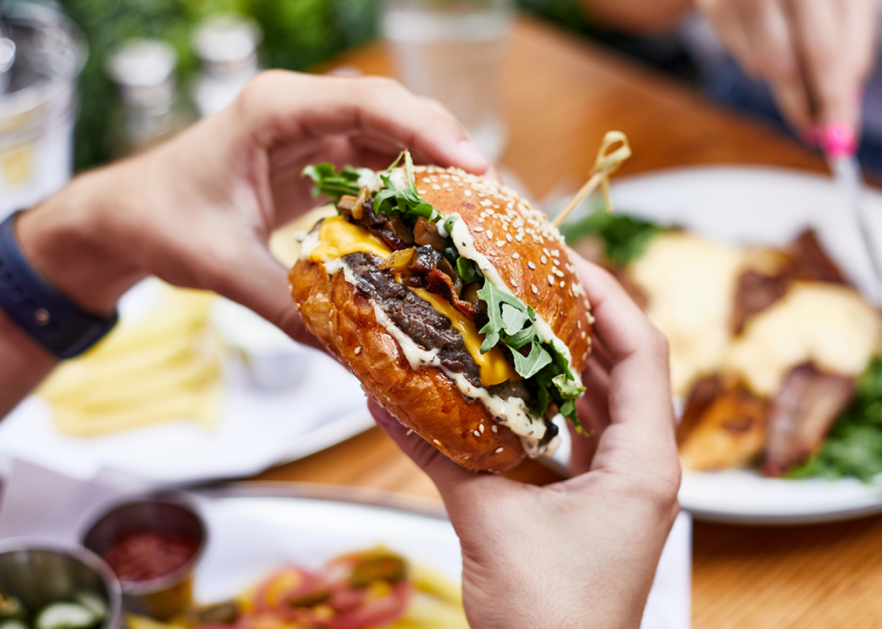 50 most popular chain restaurants in America Close up hands holding burger at outdoor restaurant table.