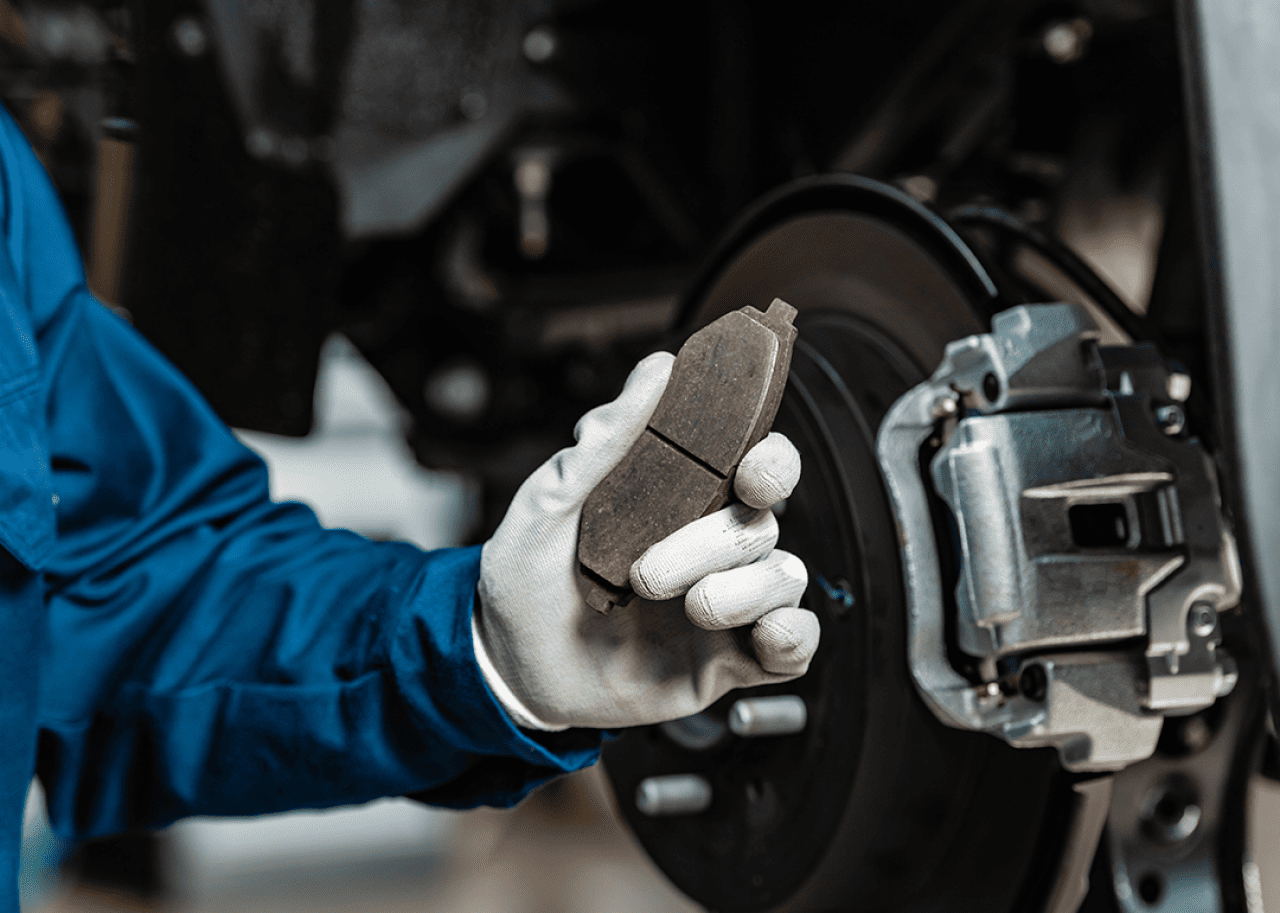 A mechanic holding a used brake pad near a wheel.