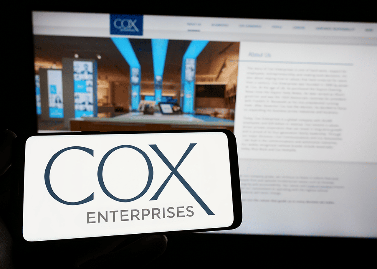 Phone with logo of Cox Enterprises Inc.on screen in front of website.
