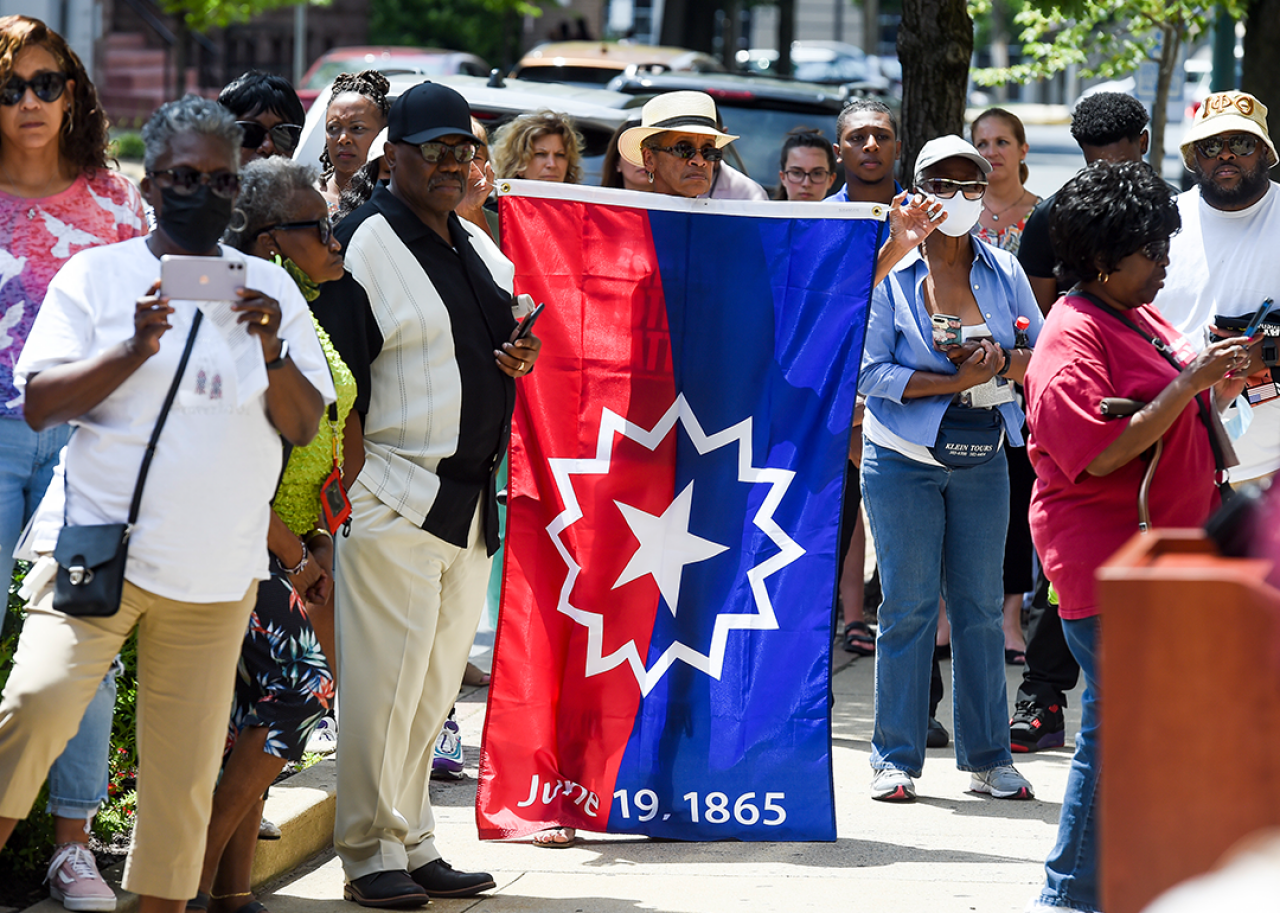 People stand during a Juneteenth flag raising ceremony.