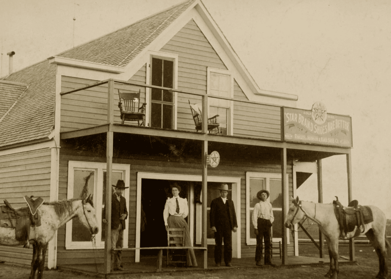 People and horses standing in front of a rural building with a sign