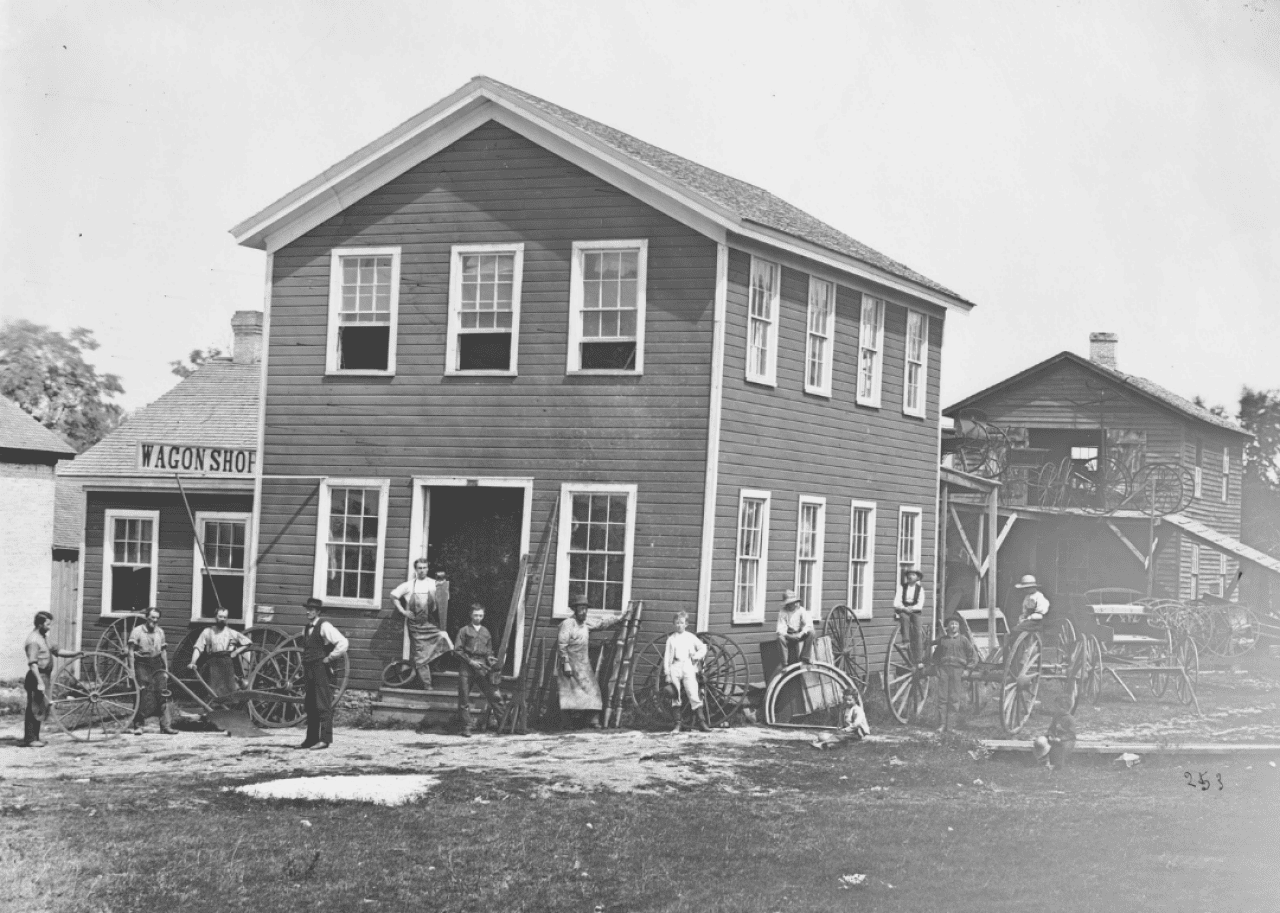 Men and boys stand in front of a wagon shop