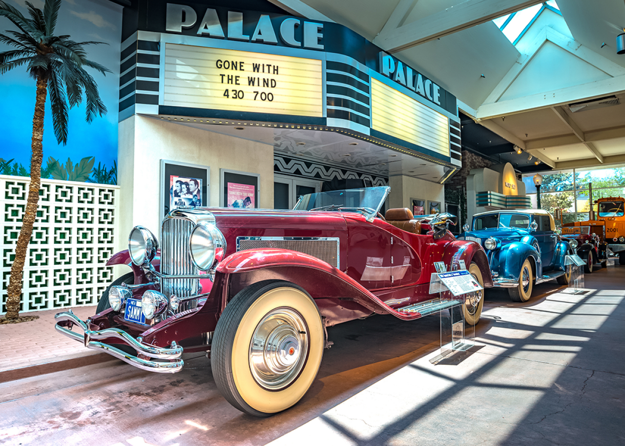 Vintage car parked under painted movie marquee.