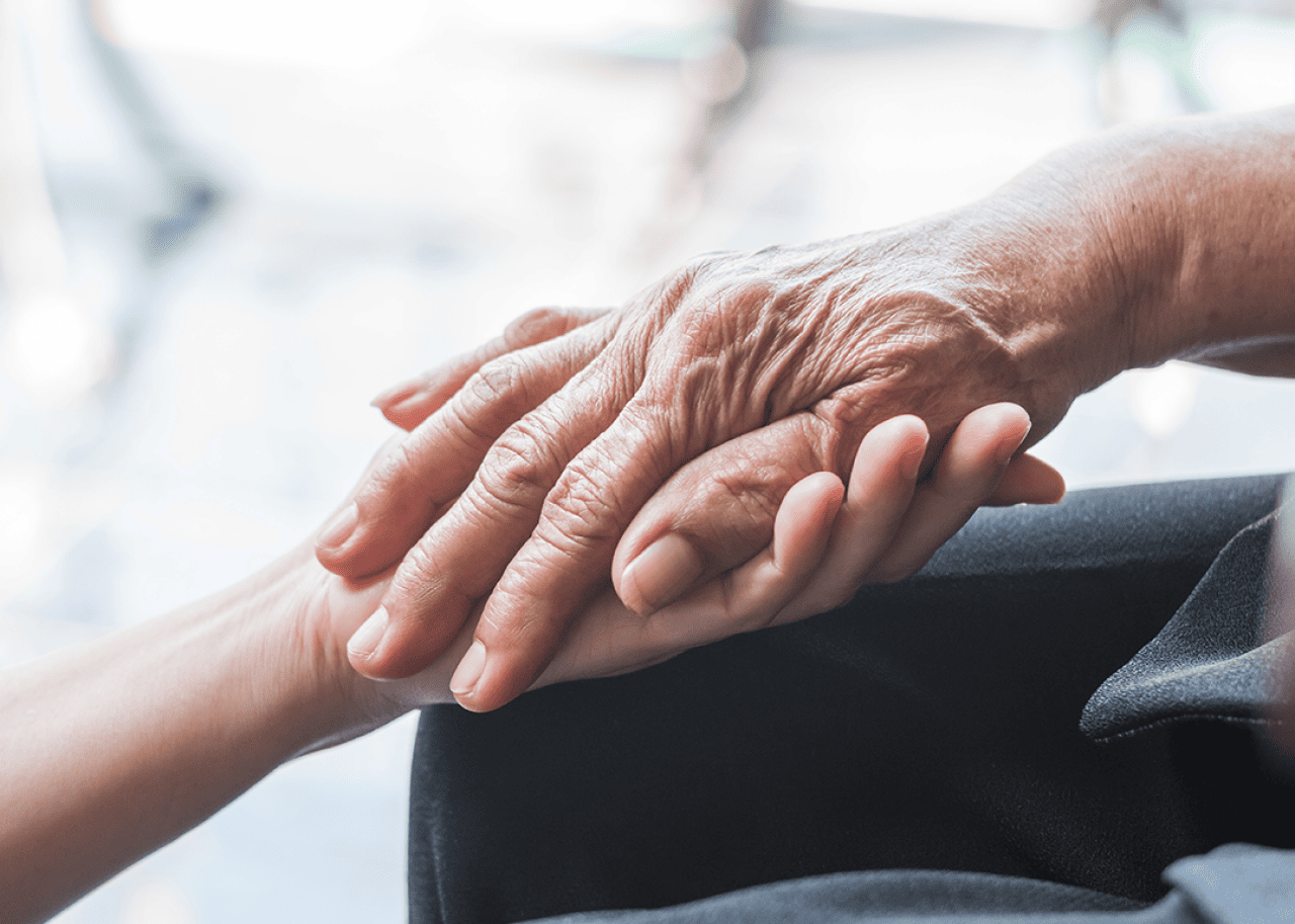 Close up caregiver holding senior hand.