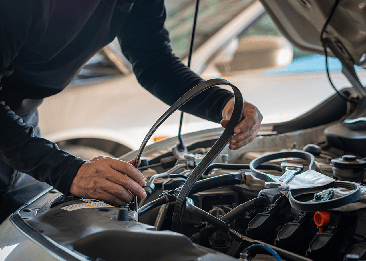 A mechanic working under the hood of a car holding a timing belt.