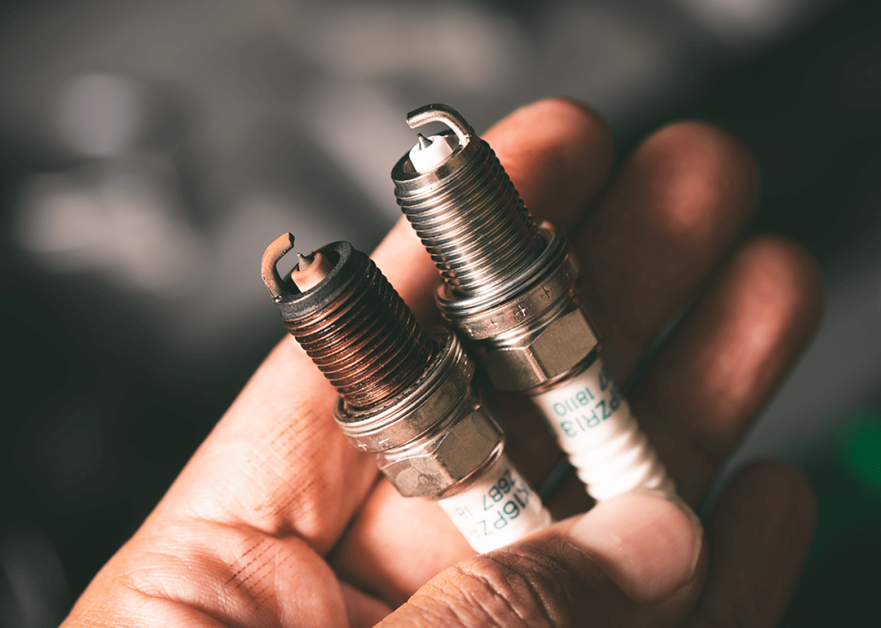 A hand holding old and new spark plugs.