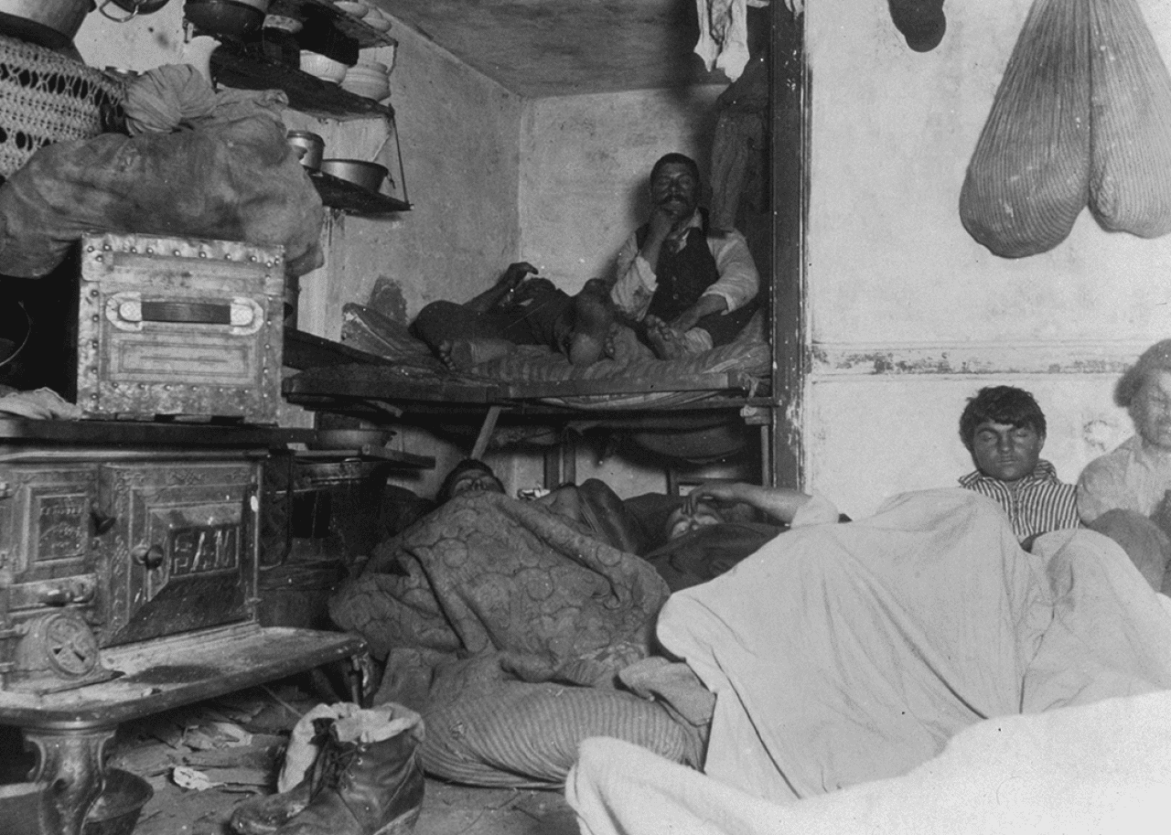 Lodgers in a crowded windowless tenement photographed at night.
