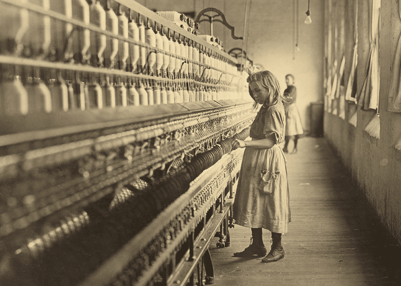 A young girl tends the spinning machine at a cotton mill.