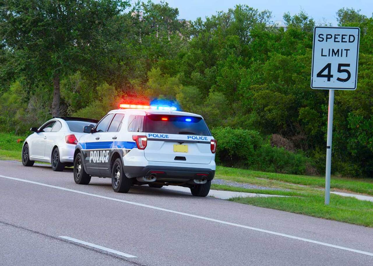 A highway patrol pulling over driver next to speed limit sign.