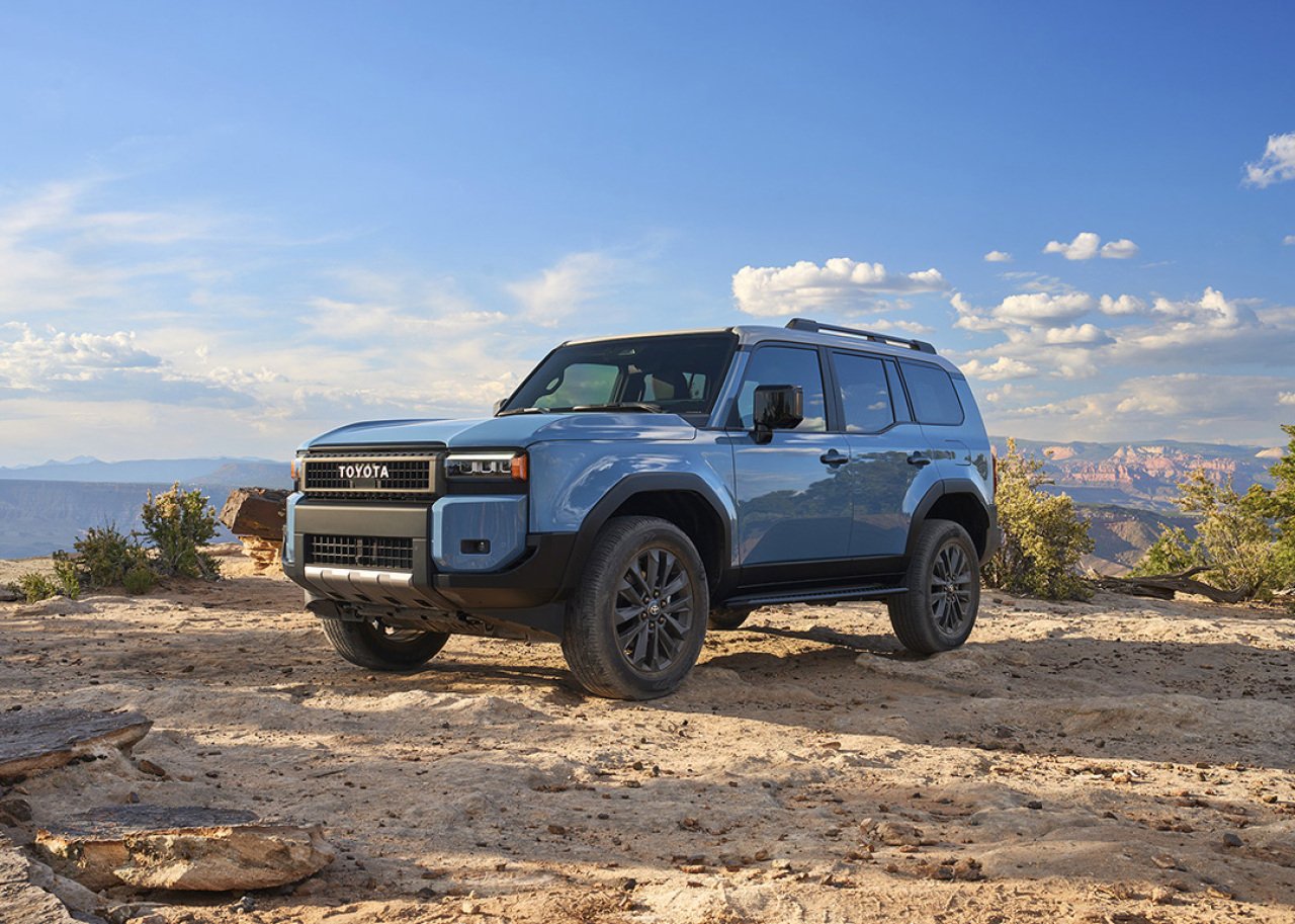 Blue Toyota Land Cruiser parked on rocky dir with sky in background.