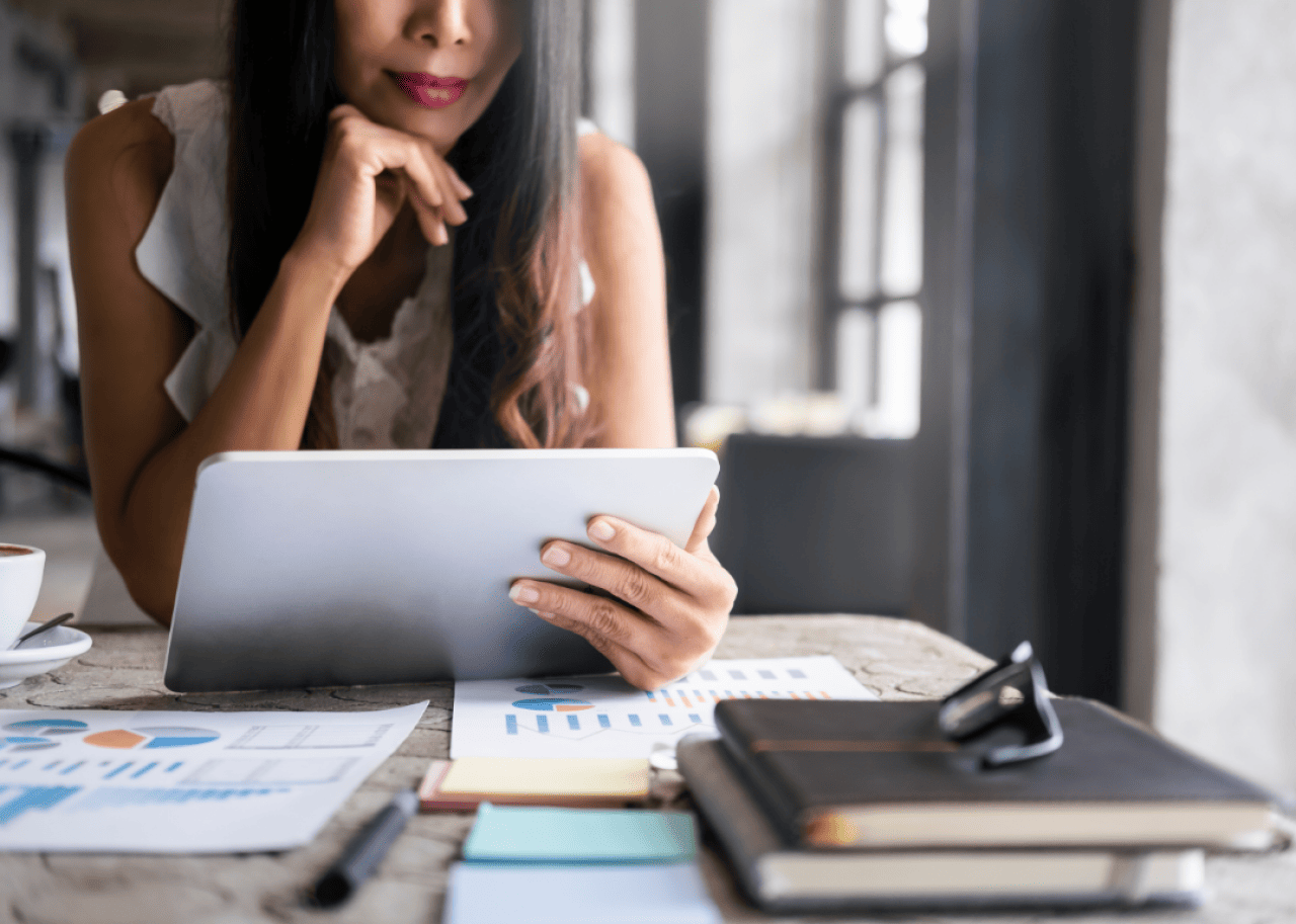 A woman seated at a desk considering investment options on a tablet.