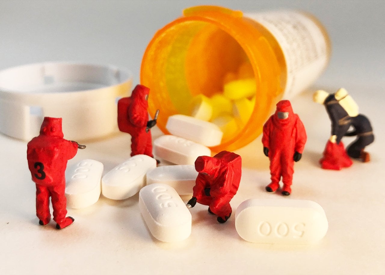 Spilled opioid pills from the bottle and miniature first responders in biohazard suits are investigating it.