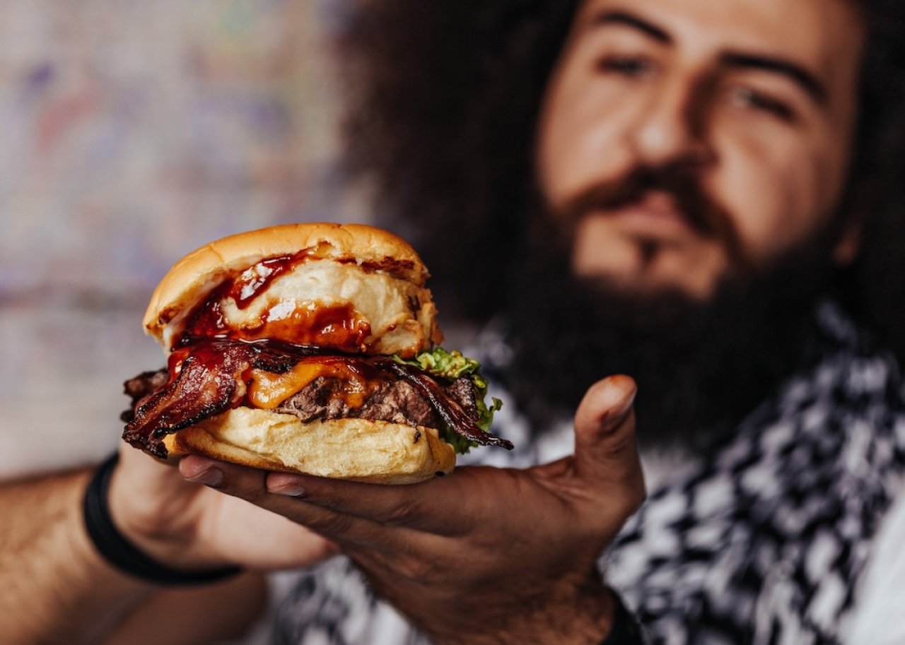 The most caloric burgers at 20 fast-food chains Curly hipster holding craft mouth-watering bacon and angus beef burger.