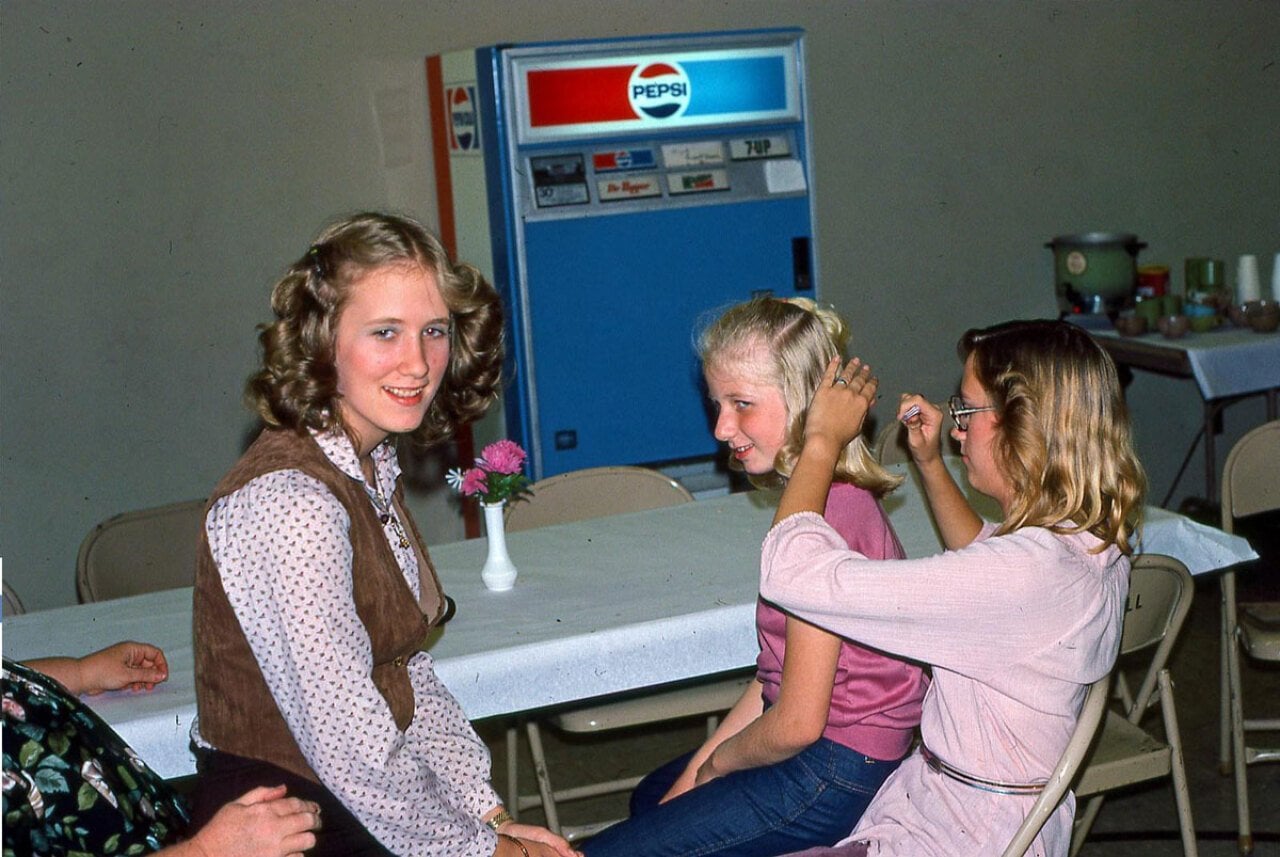 Three girls (and a fourth person mostly off-camera) sitting in a cafeteria