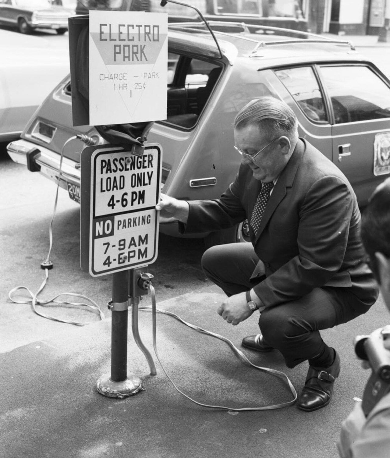 Man kneeling next to a sign that reads Electro Park while charging his car